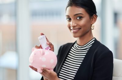 Portrait of an attractive young businesswoman putting money inside her piggy bank at work.